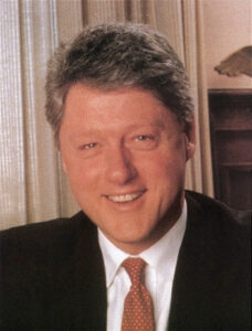 President Bill Clinton half-length portrait seated at desk facing front color 1